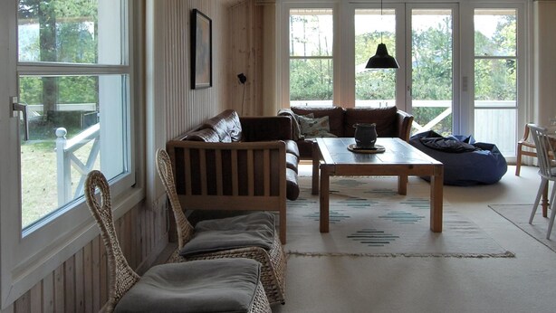 Una sala de estar acogedora con techo de madera, ventanas amplias, un sofá, una mesa y un sillón orejero azul.