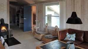 Un salón acogedor con chimenea, muebles de mimbre, un sofá de cuero y un amplio ventanal.