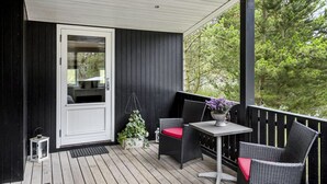 A covered porch with a white door, wicker furniture with red cushions, and a small table with a potted plant.
