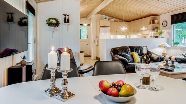 A modern living room with a dining table set for two, featuring candles, fruit, and wine glasses.
