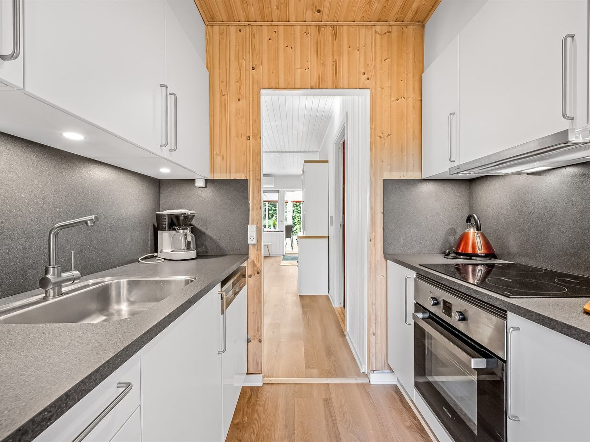 A modern kitchen with white cabinets, a stainless steel sink, a kettle, and an oven.