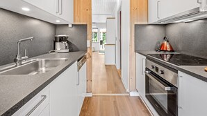 A modern kitchen with white cabinets, a stainless steel sink, a kettle, and an oven. - "Dorthe" - 300m to the fjord by Interhome (Tarm)