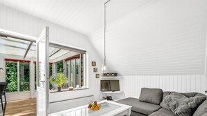 A modern living room with a white sofa, a glass coffee table, and a TV. There is a large window with a view of greenery outside. - "Dorthe" - 300m to the fjord by Interhome (Tarm)