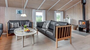 En hyggelig stue med en sofa, et sofabord med frugt og en brændeovn.