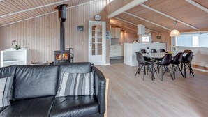 En rummelig opholdsstue med pejs, et spisebord med stole og et køkken i baggrunden.