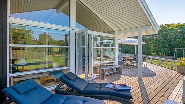 Una terrazza coperta all'aperto con poltrone relax e un tavolo, ampie finestre e vista sul verde circostante.