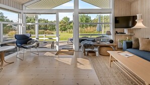Un soggiorno spazioso con soffitto alto, ampie finestre, un divano confortevole, una televisione e un'area pranzo con tavolo e sedie.