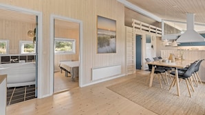 Un interno moderno caratterizzato da pareti in legno, una zona pranzo con tavolo e sedie, una cucina con lavello e piano di lavoro, e un'ampia finestra vista su vegetazione.