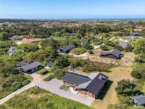 An aerial view of a residential area with houses, a large building with a sloped roof, and a clear view of the coastline.
