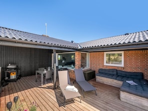 Une terrasse couverte équipée d’un barbecue, d’un coin salon et offrant une vue sur le jardin arrière.
