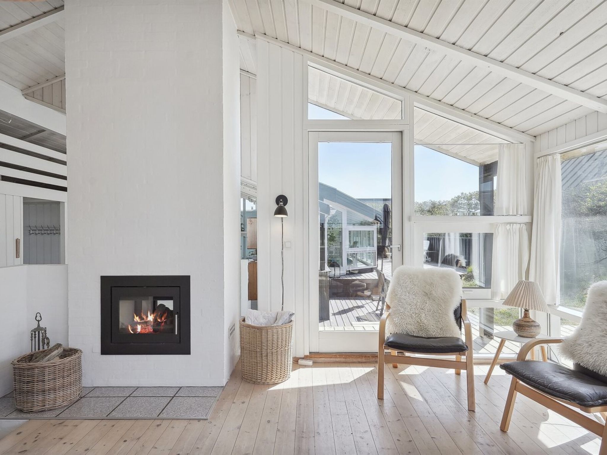En moderne stue med pejs, fletkurve og udsigt til naturen gennem store vinduer.
