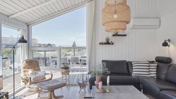 Ett rymligt vardagsrum med ett stort fönster, en svart lädersoffa, ett träbord och en hänglampa i rotting.