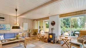 A cozy living room with a fireplace, wooden furniture, and large windows offering a view of the outdoors.