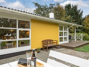 Un edificio amarillo con amplias ventanas, una terraza y asientos al aire libre.