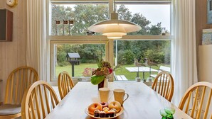 A dining area with a wooden table, chairs, a vase with flowers, and a view of the garden through large windows.