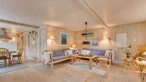 A spacious living area with a wooden floor, a blue sofa set, a wooden coffee table, and a dining area with a wooden table and chairs.