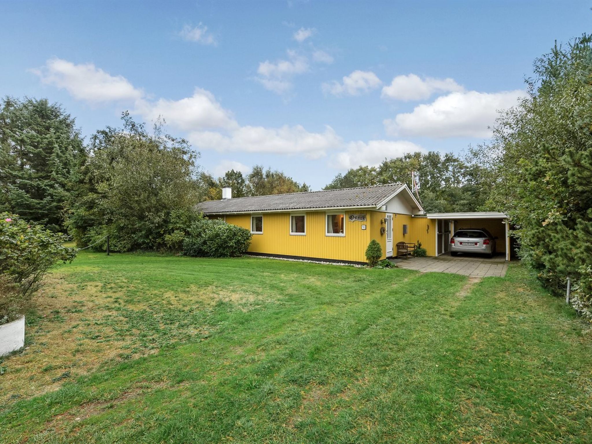 Ein gelbes Einfamilienhaus mit Garage, umgeben von einem gepflegten Rasen und Bäumen.