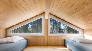 Ein Zimmer mit zwei Betten, Holzwänden und großen Fenstern mit Blick auf einen Wald.
