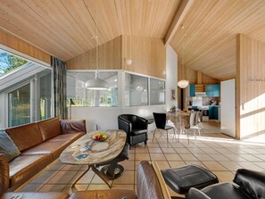 Un interior moderno con techo de madera, una zona de comedor con mesa de mármol, un sofá y una cocina al fondo.