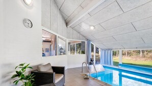 Ein überdachter Poolbereich mit Rattanmöbeln, einer Uhr und Blick ins Freie.