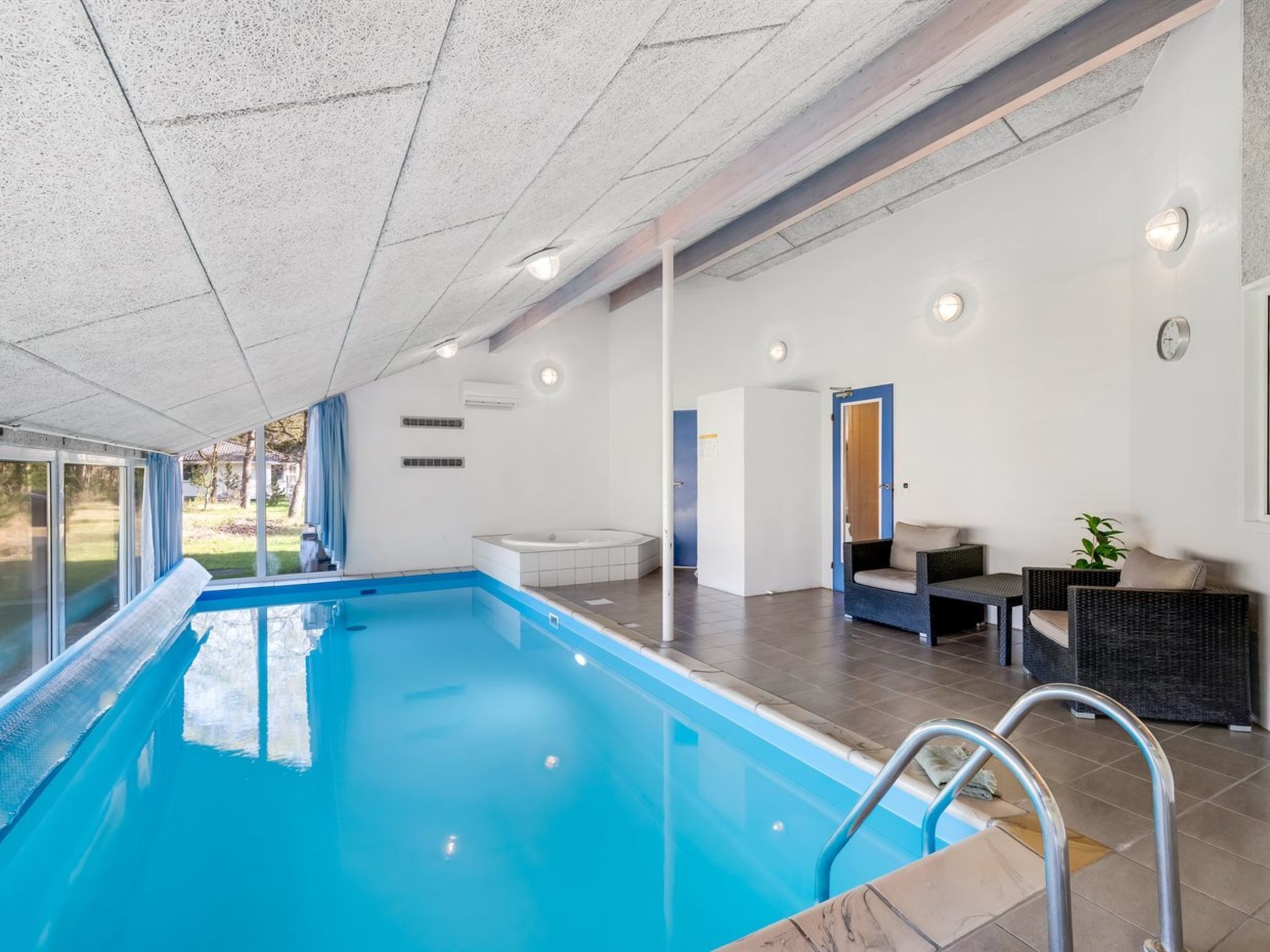 A swimming pool with a clear view of the surrounding area, including a seating area with a table and chairs, and a door leading to another room.