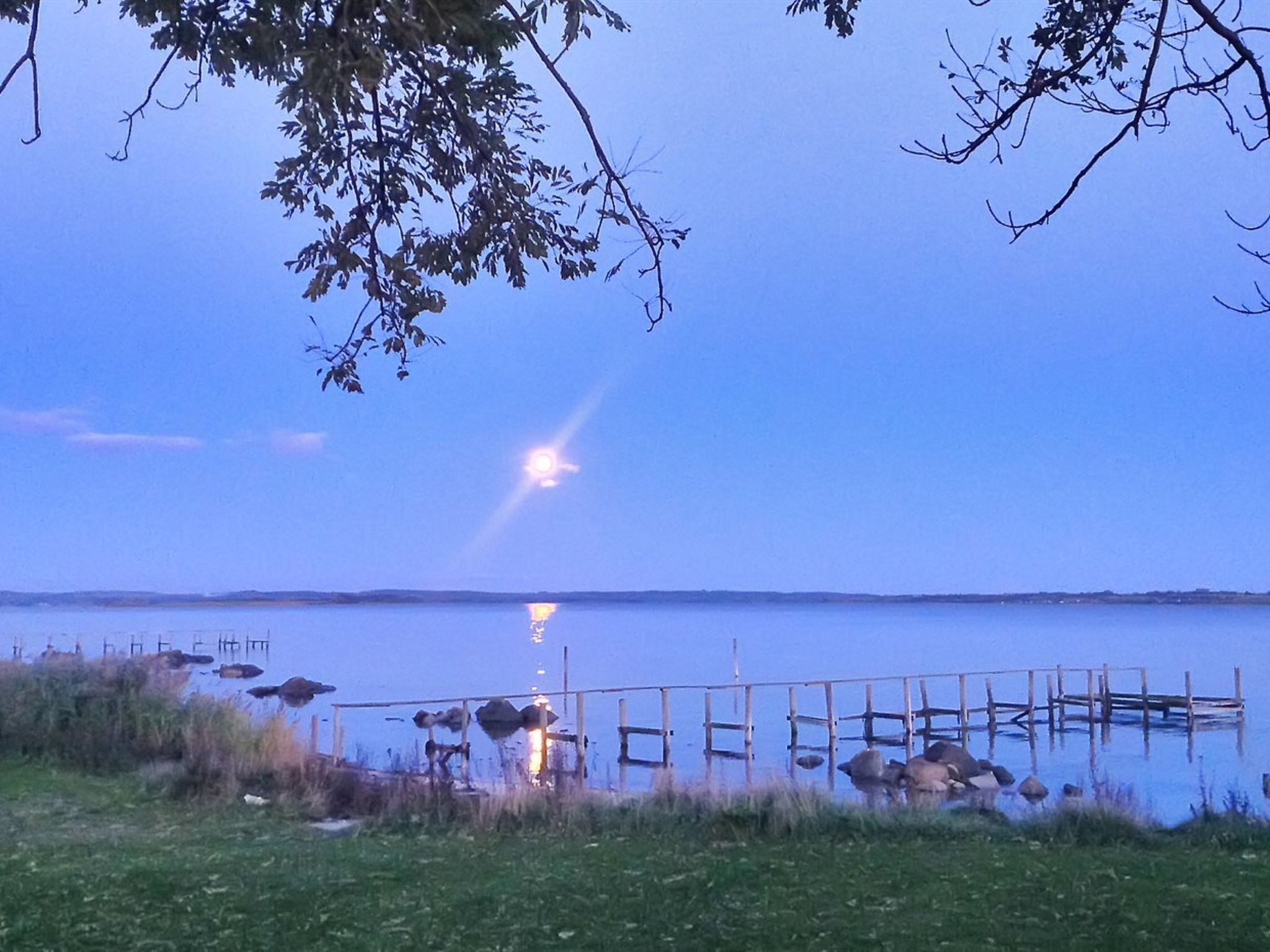 A calm lake at dusk with a wooden dock extending into the water.