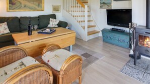Ett mysigt vardagsrum med en soffa, ett soffbord, flätade stolar, en tv, en öppen spis och en trappa.