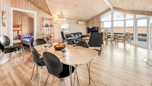 Una habitación amplia con techo alto, paredes de madera, un comedor con mesa y sillas, un sofá y un televisor.