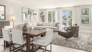 A modern living room with a dining area, large windows, and artwork on the walls. - The Boardroom Residence at Peninsula Village (Newport Beach)