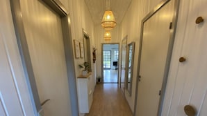 Een gang met houten vloer, witte muren en deuren aan weerszijden. Er hangen ingelijste foto's en staat een kleine plant op een plank.