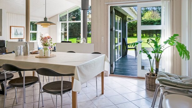 A modern kitchen with a large dining table, chairs, and a view of the garden through the sliding glass door.