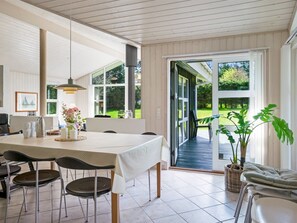 A modern kitchen with a large dining table, chairs, and a view of the garden through the sliding glass door.