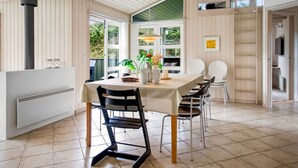 A dining area with a table set for four, surrounded by chairs, a large window with a view of greenery, and a ceiling with exposed wooden beams.