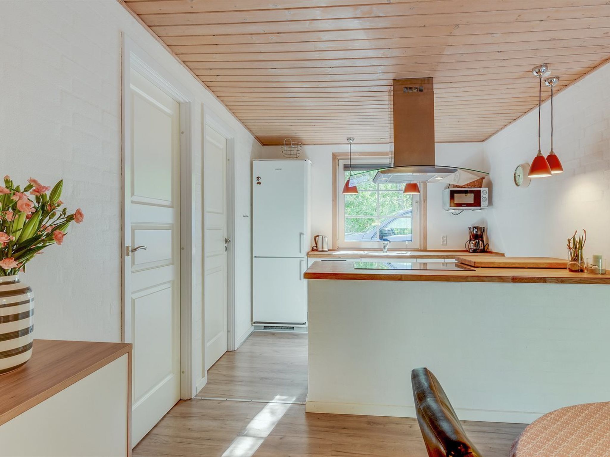 A modern kitchen with wooden flooring, a central island, and pendant lighting.