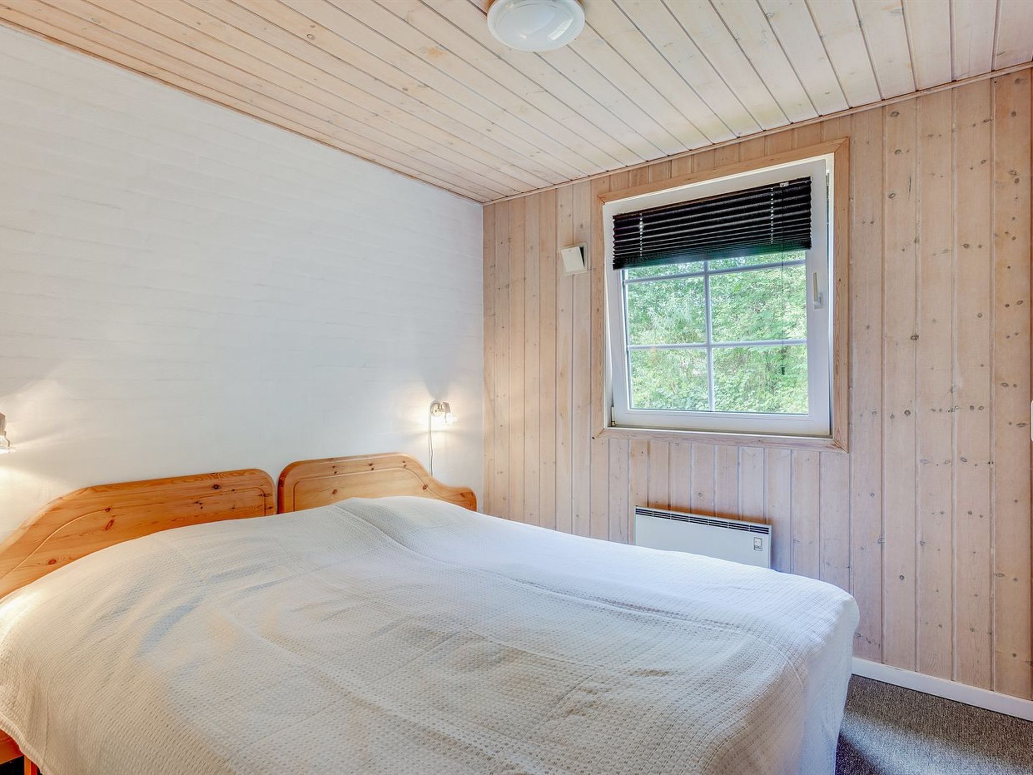 Ein Schlafzimmer mit Holzbalkendecke, einem großen Fenster und einem Bett mit weißer Decke.