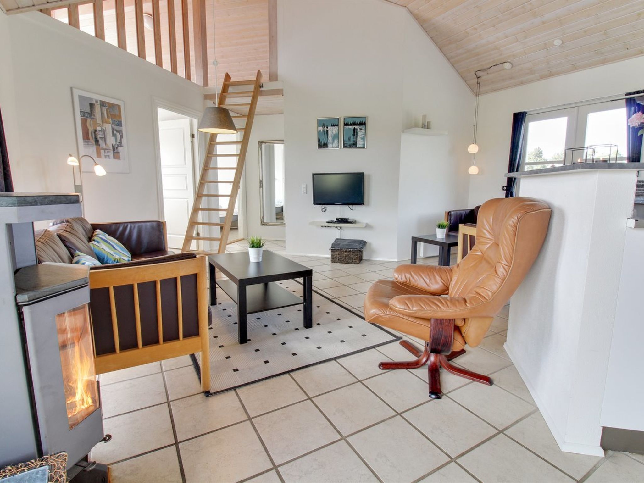 A cozy living room with a fireplace, a sofa, a leather chair, a TV, and a staircase leading to an upper level.