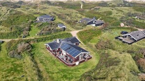 Ein Küstenwohngebiet mit Häusern, umgeben von grasbewachsenen Dünen und einem Strand im Hintergrund.