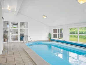 An indoor swimming pool with clear glass doors, a tiled floor, and a view of greenery outside.