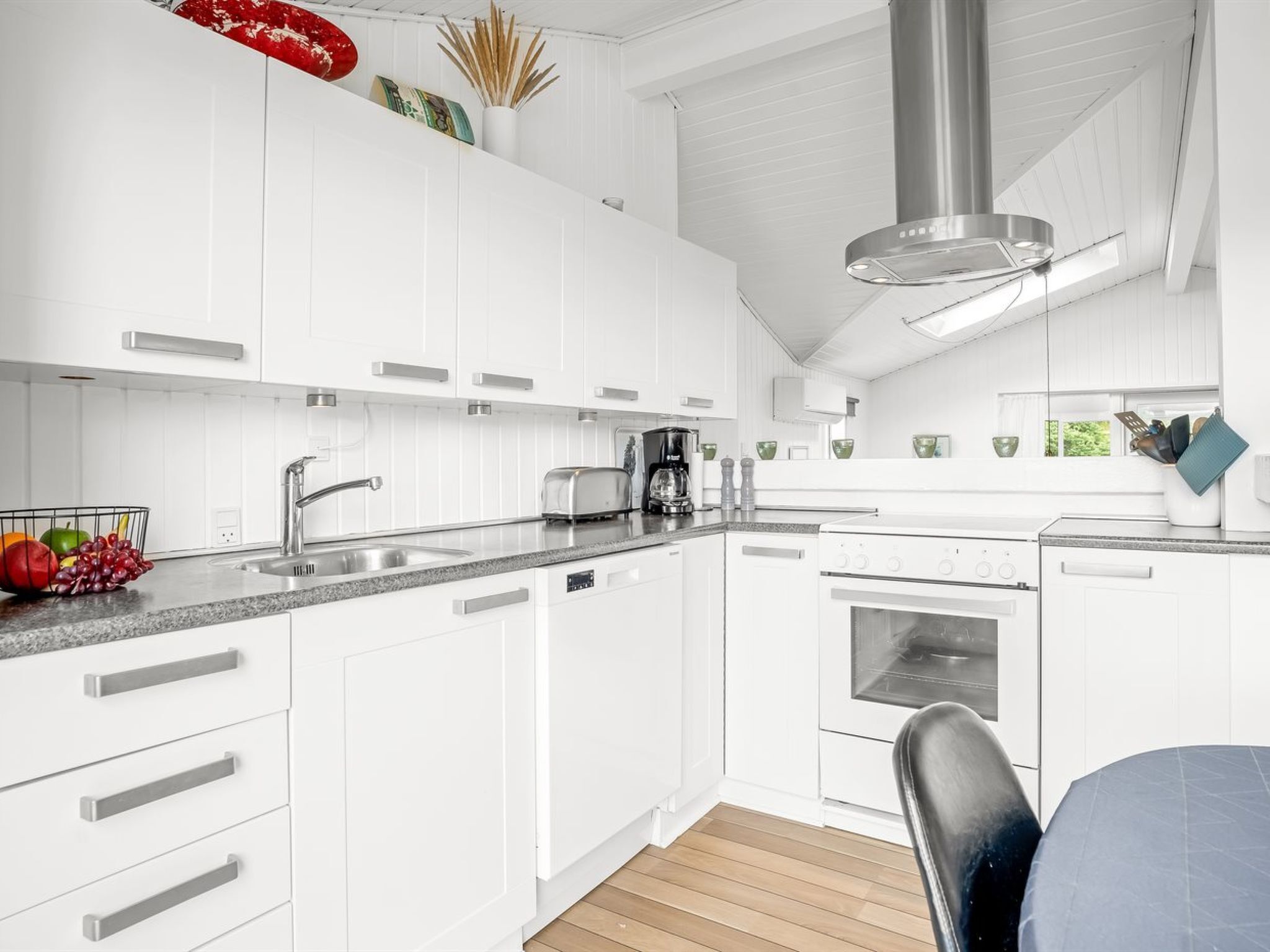 Una cocina moderna con muebles blancos, una campana extractora de acero inoxidable, horno empotrado y encimera de granito.