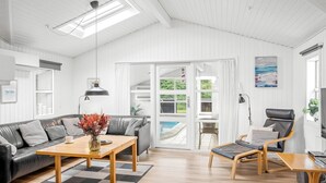 Ein modernes Wohnzimmer mit Sofa, Couchtisch und Sessel, Blick auf einen Pool und einer Decke mit Dachfenstern.
