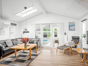 A modern living room with a sofa, coffee table, and armchair, a pool view, and a ceiling with skylights.