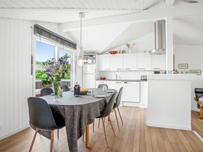 A modern kitchen with white cabinetry, a dining area with a round table, and a view of greenery outside.