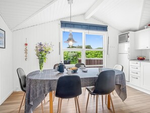 A dining area with a table set for four, a vase of flowers, and a view of greenery outside.