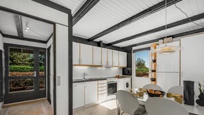 A modern kitchen with white cabinets, a dining area with a table and chairs, and a view of greenery outside. - "Sigbrith" - 350m to the fjord by Interhome (Tarm)