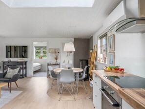 Een moderne keuken met een inbouwoven, een eethoek met een ronde tafel en stoelen, en een groot raam dat zorgt voor natuurlijk licht.