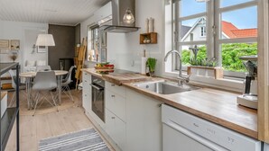 Eine moderne Küche mit großem Fenster, einem Essbereich mit Tisch und Stühlen sowie Blick auf ein Haus und einen Garten.