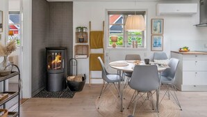 Eine moderne Küche mit einer zentralen Kochinsel, einem Essbereich mit rundem Tisch und einem eingebauten Kaminofen.