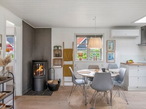 Een moderne keuken met een centraal kookeiland, een eethoek met een ronde tafel, en een ingebouwde houtkachel.