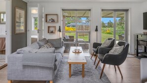 Ein modernes Wohnzimmer mit einer Couch, Sesseln, einem Couchtisch und Blick durch große Glastüren in einen Garten.