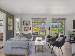 Een moderne woonkamer met een bank, stoelen, een salontafel en uitzicht door grote glazen deuren op een buitenplaats.